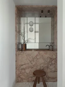 Modern bathroom with marble walls and floor, featuring a sink with a faucet and a round wooden stool.