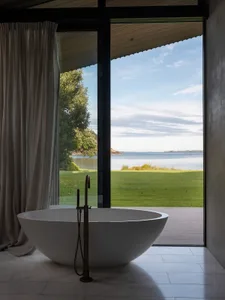 A minimalist bathroom featuring a freestanding bathtub with a beautiful coastal view through large windows.