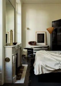 Modern, minimalist bedroom with white marble fireplace, metal furnishings, and wooden floors.