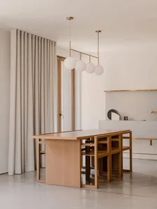 A minimalist kitchen with wooden furniture and white pendant lights hanging above.