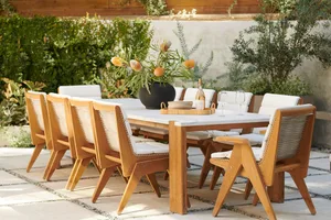 A minimalist outdoor dining set featuring wooden chairs and a marble table surrounded by lush greenery.