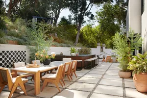 Modern outdoor dining area with concrete pavers, lush greenery, and comfortable seating.