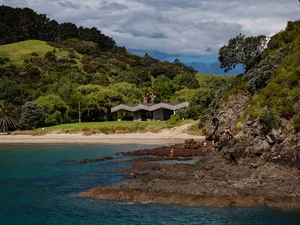 Modern beach house with concrete, wood, and tiled flooring, surrounded by lush greenery.