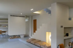 A minimalistic, modern living room with concrete walls and floors, featuring a fireplace and seating area.