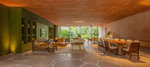 A modern living and dining room featuring concrete flooring and furniture, with greenery outside.