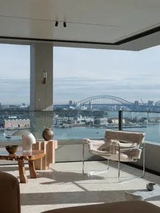 A modern minimalist living room with a view of a cityscape featuring the Sydney Harbour Bridge and the Sydney Opera House.