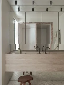 Modern minimalist bathroom with a large rectangular sink counter made of marble, a large mirror above it, and a stool underne