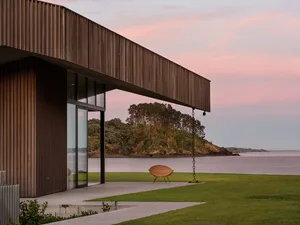 A modern residential exterior featuring a wooden beam and a view of a calm lake with a mountain in the background.