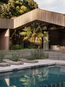 A modern residential exterior featuring wood siding and a pool area with lounge seating.