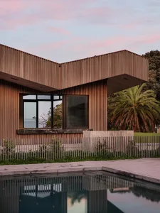 A modern residential house with wooden exterior and large windows, featuring a pool and landscaped garden.