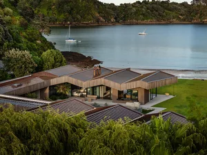 Modern residential home with wooden roofs situated by a calm lake, featuring sailboats and lush greenery.