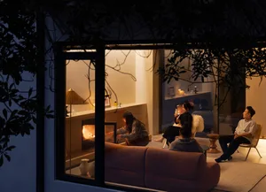 People sitting in a cozy living room at night, illuminated by warm lighting, with a fabric couch and a fireplace.