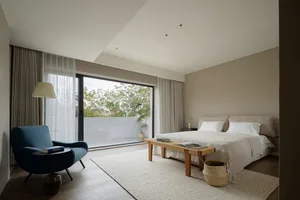 A modern minimalist bedroom with white walls, a neutral color palette, and a large window with curtains.