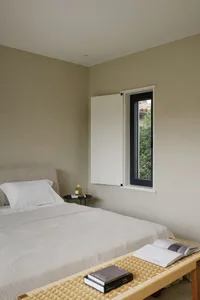 A minimalist bedroom with neutral-toned textiles and a window showing greenery outside.