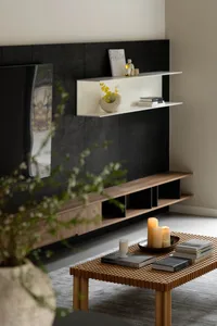 A minimalist living room featuring wooden furniture, a coffee table with candles and books, and a plant in the foreground.