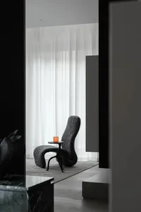 Modern living room with a black fabric chair and a lit candle on a small table.