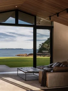 Modern living room featuring glass windows, wooden flooring, and a cozy leather sofa.