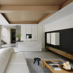 A modern living room featuring a white couch, a coffee table with candles and books, and a kitchen island with a marble count