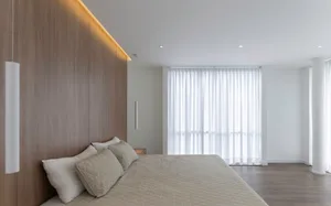 Modern minimalist bedroom with textured cotton blanket, white curtains, gray floor, and wood headboard.
