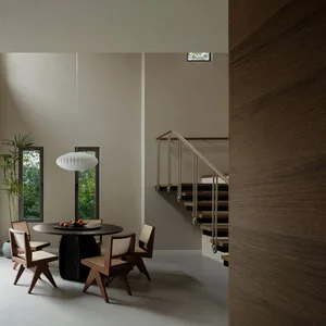 A modern minimalist dining room featuring a wooden table and chairs with a white pendant light hanging above it, set against 