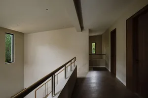 A minimalist hallway with wooden flooring and railings, featuring a small window overlooking greenery.