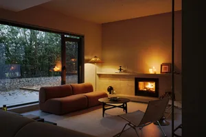A modern minimalist living room featuring a cozy fireplace and comfortable seating area with a large window overlooking natur