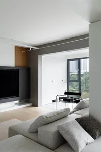 A modern minimalist living room with a large gray sofa adorned with fabric cushions, a sleek black armchair, and a large tele