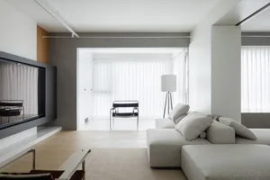 A modern minimalist living room with a neutral color palette, featuring a large sectional sofa, floor lamp, and a television.