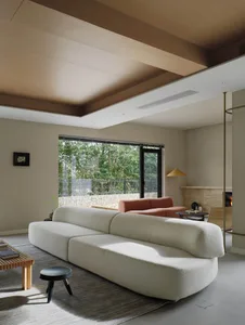 A modern residential interior living room featuring a white sofa, a wooden coffee table, a black stool, and a large window ov