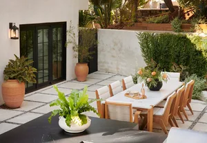 Outdoor dining terrace featuring marble dining table, concrete floor, wooden chairs, and terracotta planters with greenery.