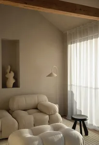 A minimalist living room features a fabric sofa, curtains, and a stool.