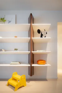 A minimalist living room featuring clean lines, white walls, and a wooden shelf with decorative items and a yellow step stool