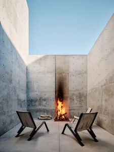 A modern concrete outdoor living space featuring a fire pit with flames