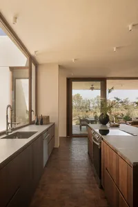 A modern, minimalist kitchen with concrete countertops and floor tiles, featuring stainless steel appliances and large window