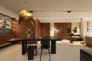 A modern dining room featuring wooden walls and furniture, with a distinctive golden pendant light hanging above a sleek dini