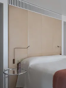 A modern minimalist bedroom with a white bed and beige leather wall paneling.