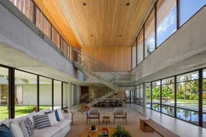 A modern minimalist living room with concrete walls and floor, featuring a white couch, grey armchairs, and a coffee table wi