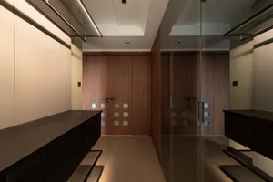 Modern, minimalist wardrobe space featuring dark wooden cabinets and glass doors with stainless steel accents.