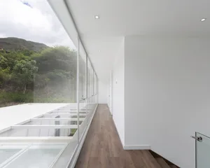 A modern residential corridor with glass walls and wooden flooring.