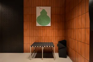 A modern restaurant interior featuring an orange tile wall and a concrete floor with a minimalist metal table and black trash