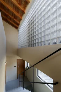 Industrial design staircase with transparent glass blocks on the wall, featuring a wooden ceiling beam and black metal railin