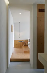 Modern minimalist bedroom with a wood platform floor, pendant light, and wooden furniture.