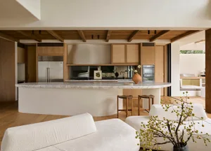 Modern minimalist kitchen featuring a curved marble countertop and wooden accents, with a lounge area and outdoor elements.