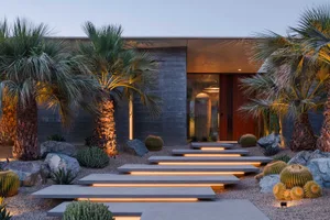 A modern architectural pathway adorned with concrete steps, illuminated by warm lights, surrounded by desert vegetation, and 