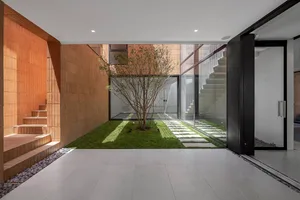A modern courtyard featuring brick walls, concrete path, and glass walls with a central tree and flooding sunlight.