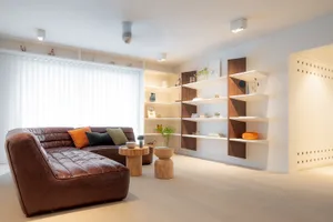 Modern living room featuring a brown leather sofa with green and orange pillows, wooden side tables, and floating wooden shel