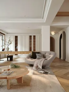 A modern living room with a Scandinavian design featuring a curved sofa, wooden coffee table, and bookcase.