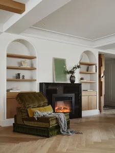 A modern living room featuring a fireplace, arched shelves, and a comfortable chair with a green throw blanket, set on a wood