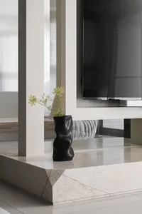 A minimalist living room with marble and concrete accents, featuring a black vase with green flowers on a marble countertop.