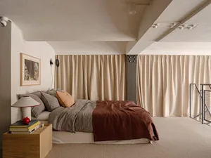Industrial bedroom with bed, pillows, and curtains beside a concrete wall and metal handrail.